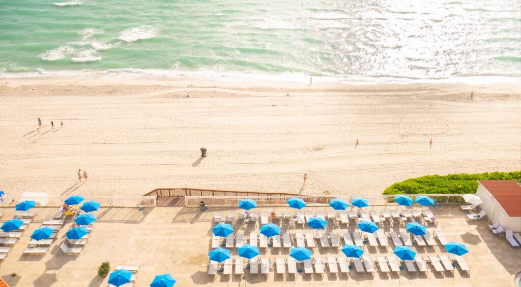 The beautiful Sunny Isles Beach in Sunny Isles Beach Florida at the Ramada Plaza by Wyndham Marco Polo Beach Resort & Hotel. Blue beach umbrellas and chairs. 